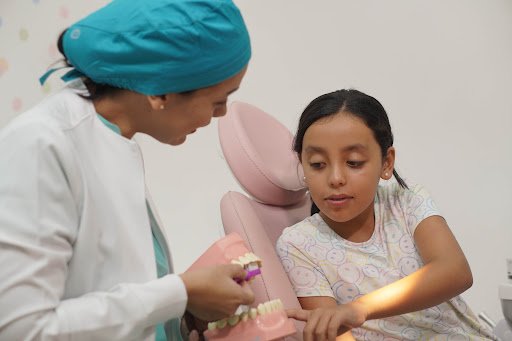 Dra. Edith González explicando modelo dental a paciente infantil en consulta clínica
